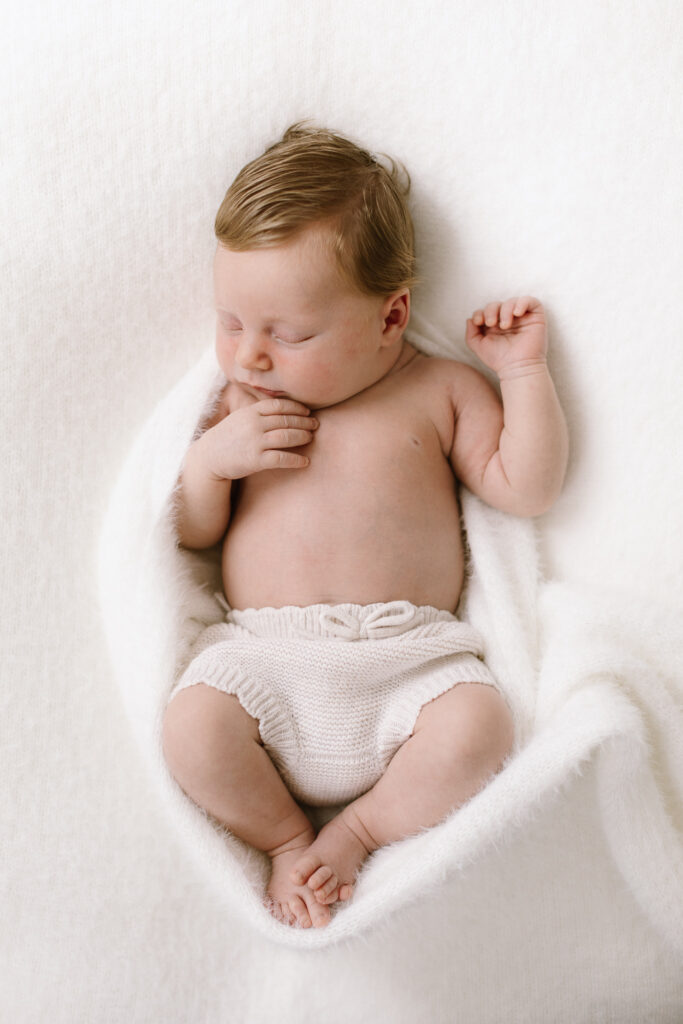 Sweet newborn asleep curled in a soft fluffy white blanket