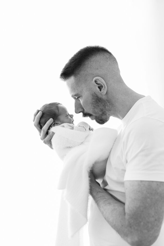 Dad holding newborn baby up to his face. Backlit black and white image