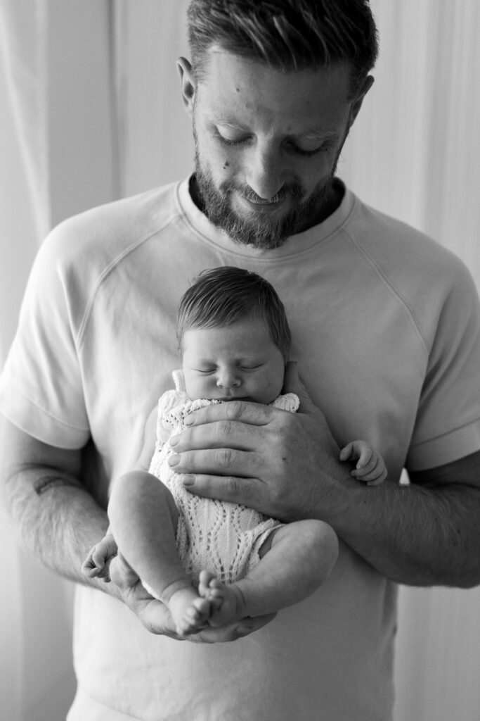 Black and white photo of a Dad and newborn baby asleep in his hands