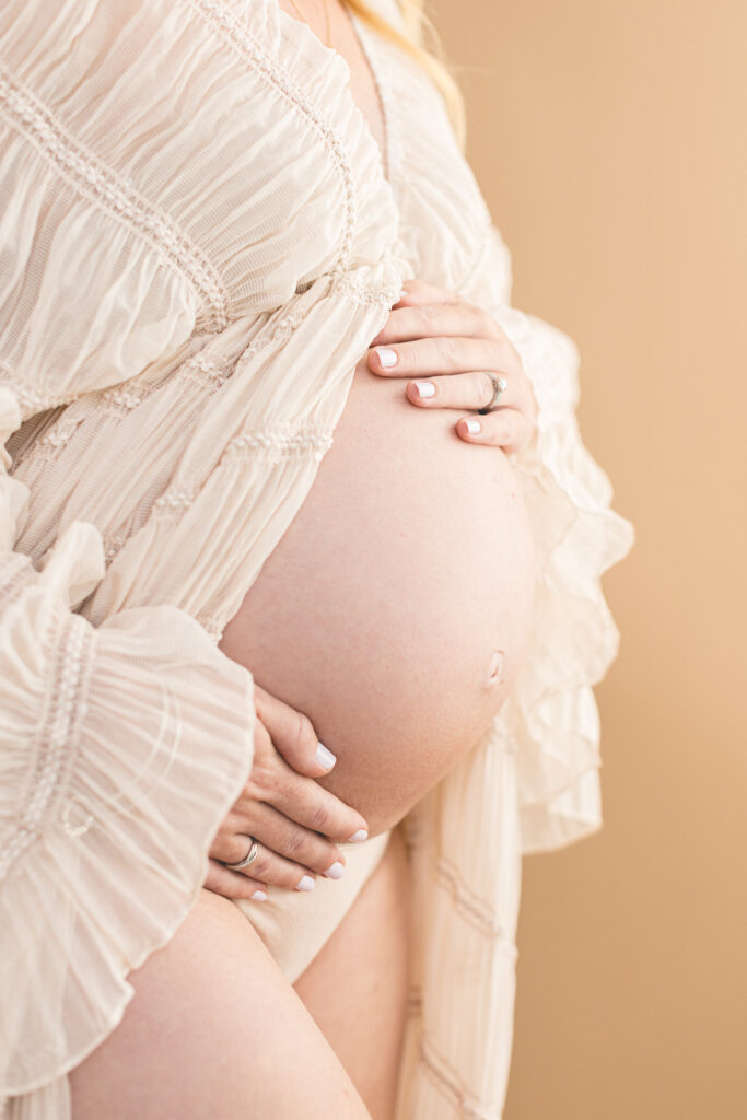 Close up of Expecting mum with long flowing dress and bump exposed. Brown photography backdrop behind