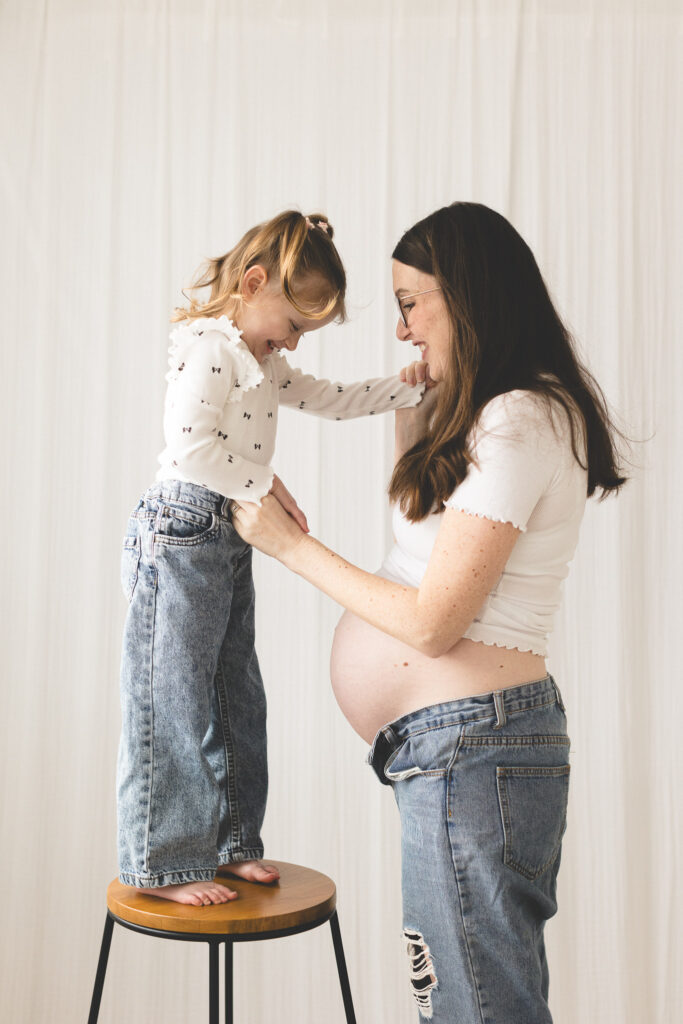 Pregnant mum with her first born daughter stood on stool, laughing together