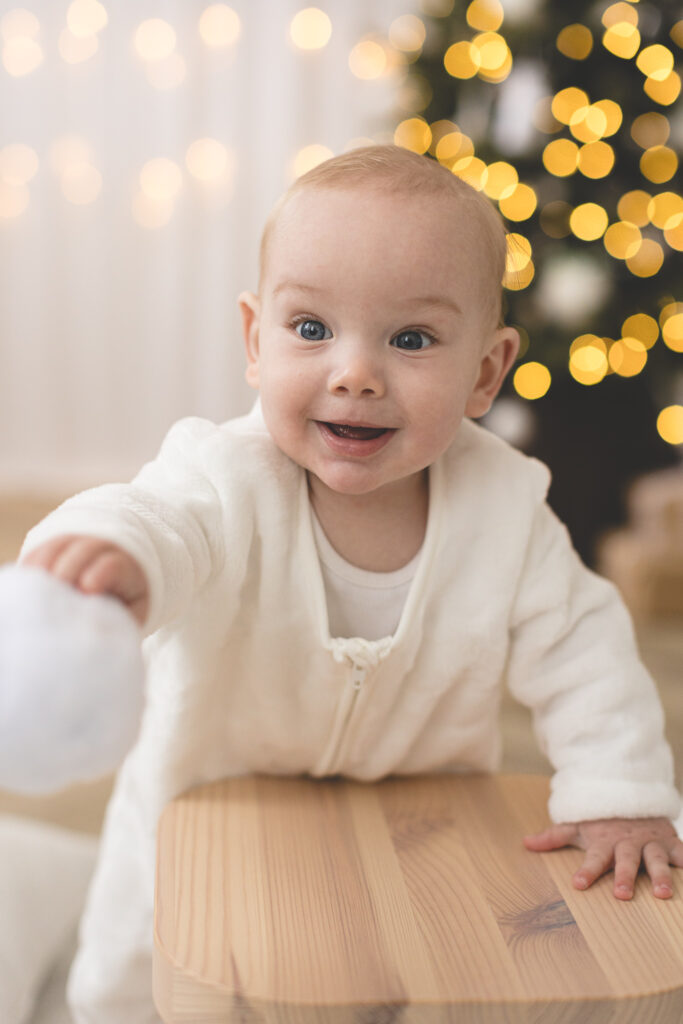 Baby with snowball in front of Christmas tree