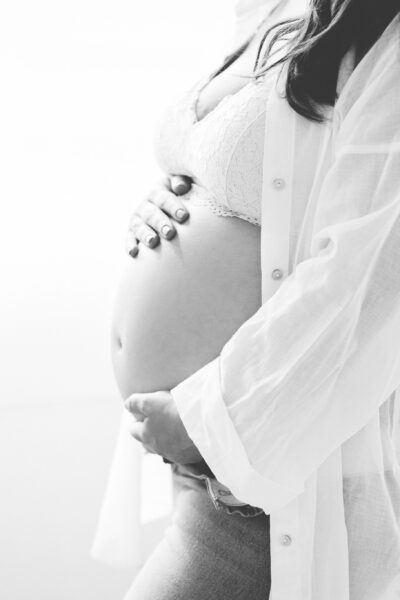 close up mums hands cradling her pregnant bump wearing jeans and white linen shirt