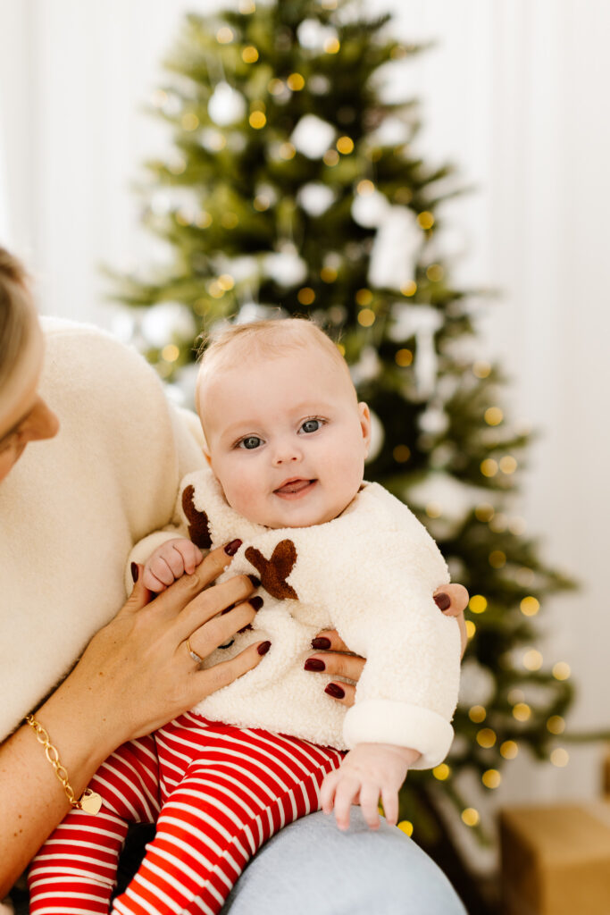 Smiling baby girl in christmas outfit by christmas tree