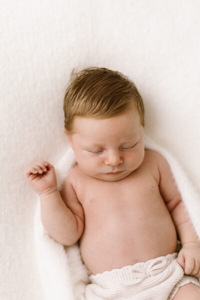 Sweet newborn asleep curled in a soft fluffy white blanket