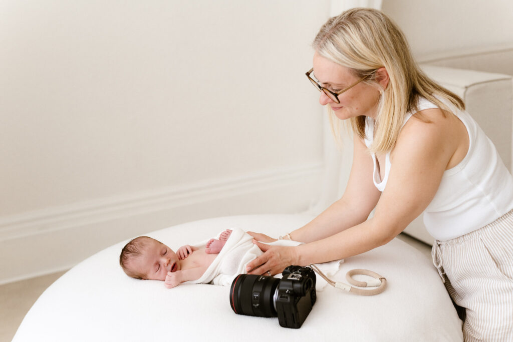 Photographer wrapping a newborn baby in blanket with camera next to them on the posing bean bag
