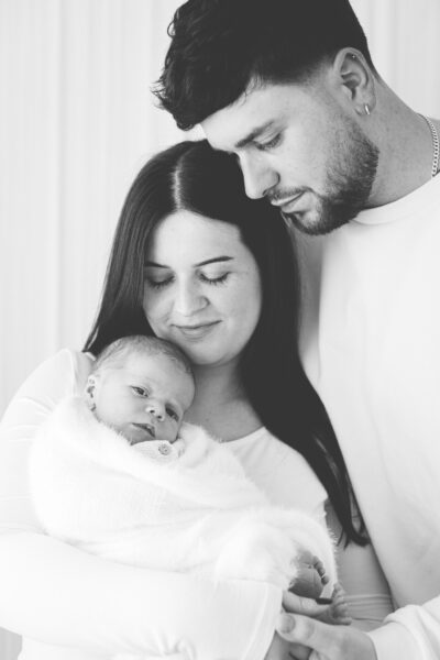 Newborn with new parents gazing down at baby wrapped in blanket